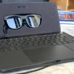 Gafas inteligentes Zero UI en estuche con teclado portátil sobre mesa de mármol – tecnología sin pantallas